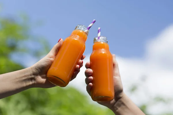 Апельсиновый свежий детоксикационный напиток в руках девушек над голубым небом — стоковое фото