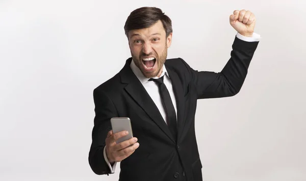 興奮したビジネスマンは、拳を振る携帯電話を保持して叫ぶ、スタジオショット — ストック写真