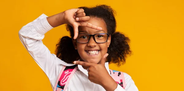 Usmívající se dívka černochů s pohledem přes prsty rám, žluté pozadí — Stock fotografie