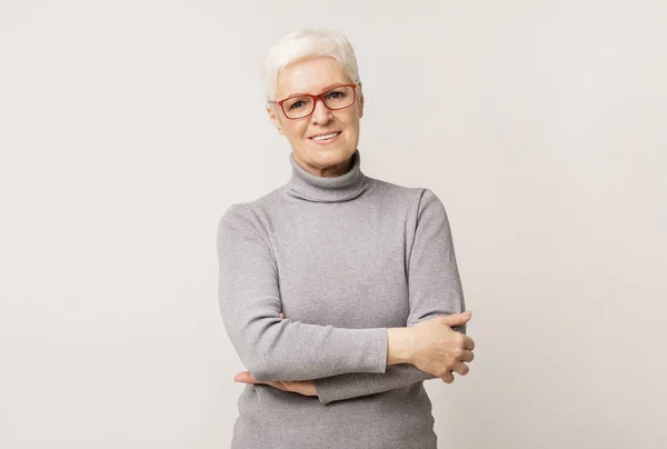 Trygg äldre kvinna i glas stående med hopfällda armar — Stockfoto