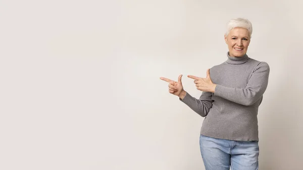 Beautiful elderly woman pointing away at free space — Stock Photo, Image