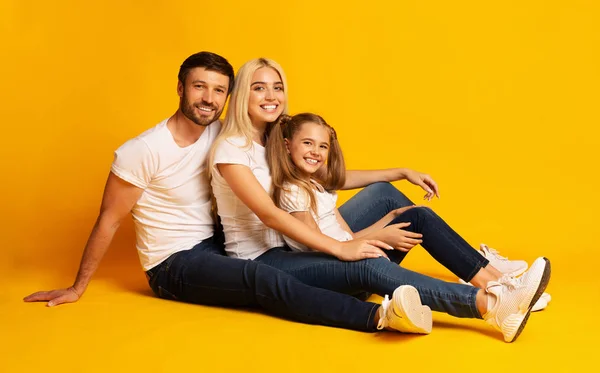 Neşeli ebeveynler ve küçük kızı katta oturan, sarı arka plan — Stok fotoğraf