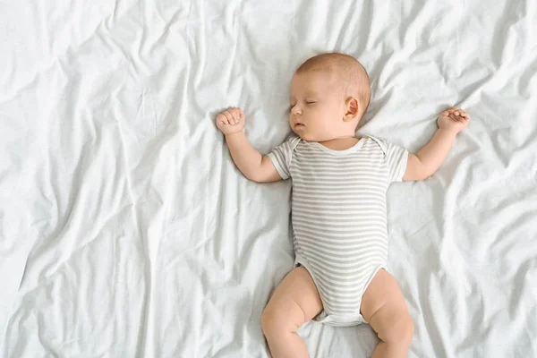 Lindo bebé en traje de cuerpo rayado durmiendo en la cama —  Fotos de Stock