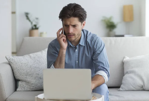 Bezorgde man praten op mobiele telefoon zittend op laptop indoor — Stockfoto