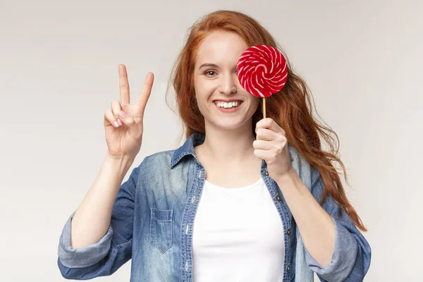 Vacker leende flicka som håller Lollipop på pinne och visar v-Sign — Stockfoto