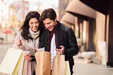 Heyecanlı çift açık havada alışveriş torbaları içine bakıyor