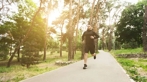 Entrenamiento matinal. Hombre deportivo trotando en el carril en el parque de la ciudad —  Fotos de Stock