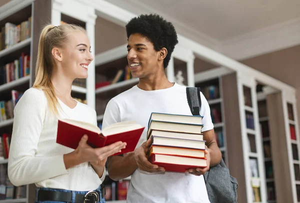 Multi etnische tiener paar praten over boek in de bibliotheek — Stockfoto