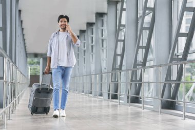 Genç turist telefonda konuşuyor, havaalanında bagajda yürüyor