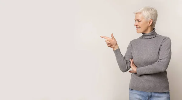 Lachende Senior dame kijkt en wijst opzij bij Kopieer ruimte — Stockfoto