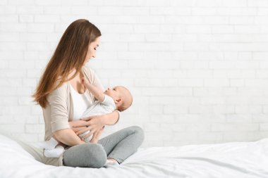 Yeni doğan oğlunu tutan genç anne, bebeği yatakta dolandırıyor