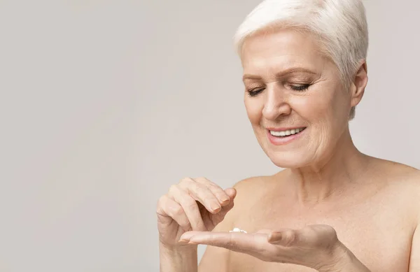Donna anziana felice che applica la crema antirughe per pelle — Foto Stock