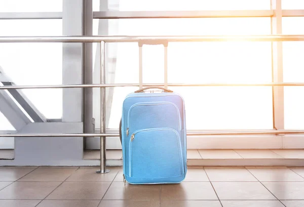Blauer Koffer am Flughafengebäude, gegen Fenster mit Sonnenfackel — Stockfoto