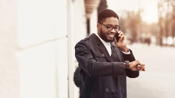 Joven hombre de negocios hablando por teléfono celular y mirando el reloj —  Fotos de Stock