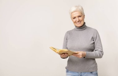 Güzel yaşlı bayan kitap tutan ve kameraya gülümseyen
