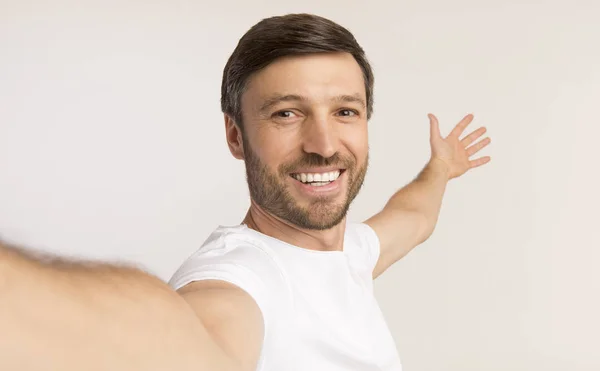 Uomo che prende selfie mostrando qualcosa dietro di lui, sfondo bianco — Foto Stock