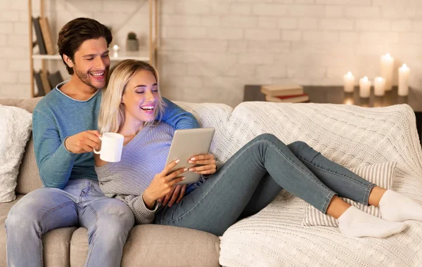 Pareja alegre usando la tableta que mira la película que relaja en el sofá interior —  Fotos de Stock