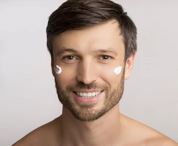 흰색 배경을 통해 얼굴에 안티 에이징 크림을 적용하는 남자 — 스톡 사진