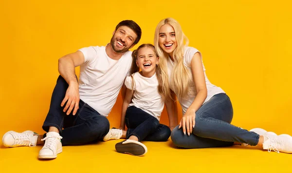 Dreiköpfige Familie sitzt zusammen auf dem Boden vor gelbem Hintergrund — Stockfoto