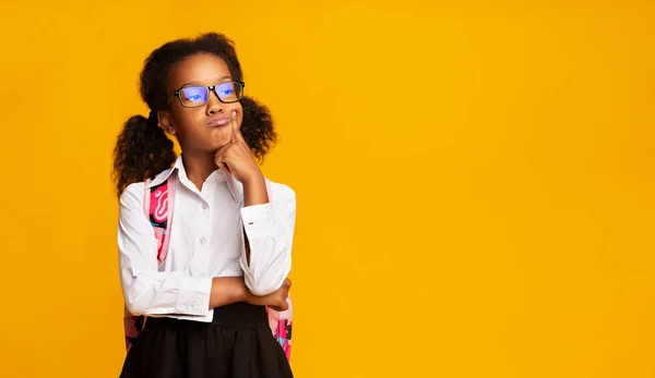 Грустная чернокожая школьница думает, касаясь подбородка на желтом фоне — стоковое фото