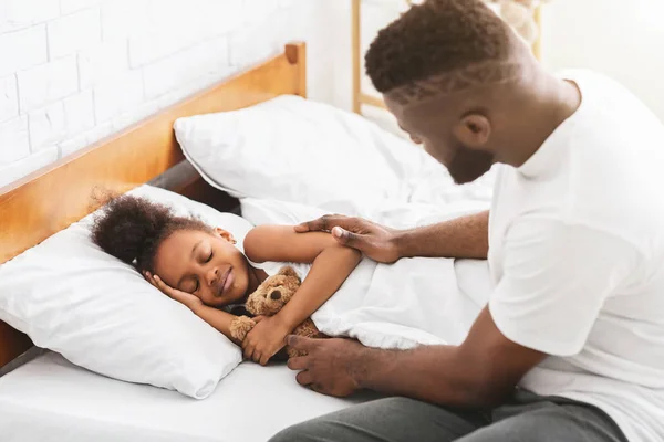 Caring african dad putting his little daughter to sleep