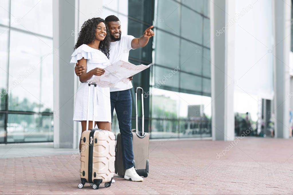 Young black couple planning vacation route, standing with map at airport