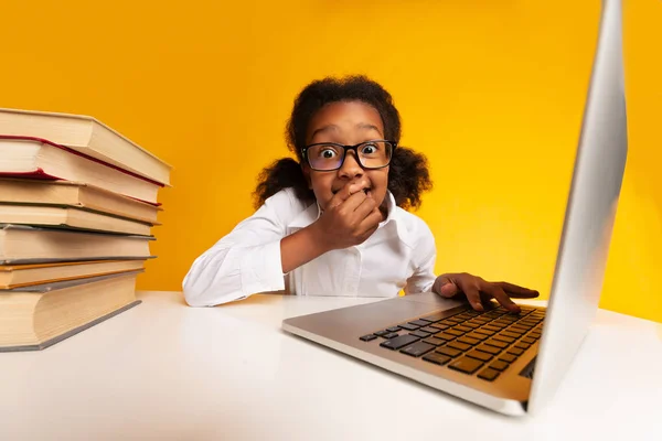 Шокована школярка сидить на ноутбуці, покриваючи рот, студійний знімок — стокове фото