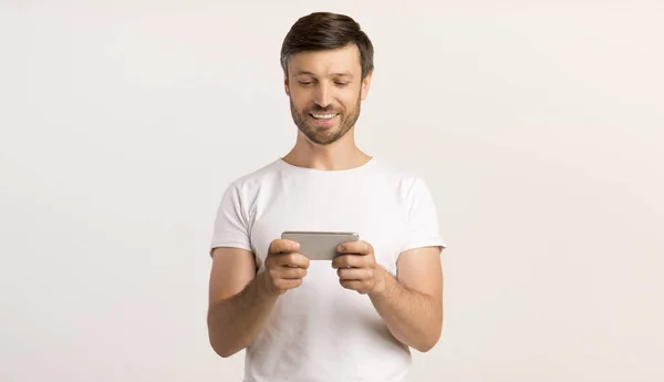 Mann mit Mobiltelefon spielt Spiele oder SMS, weißer Hintergrund — Stockfoto