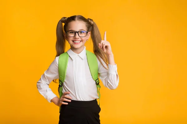 Pequena estudante apontando o dedo para cima sobre fundo amarelo, Studio Shot — Fotografia de Stock