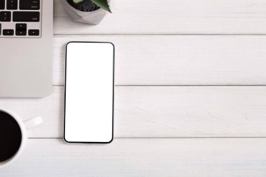 Boş akıllı telefon, dizüstü bilgisayar ve bir fincan kahve içeren ofis masası