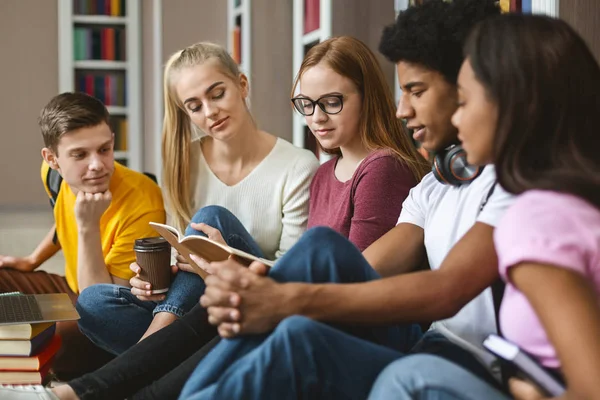 Cinco compañeros leyendo notas de clase, sentados en el piso de la biblioteca — Foto de Stock