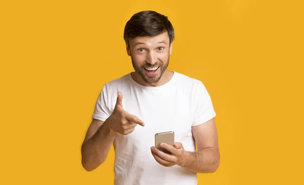 ชายชี้ไปที่โทรศัพท์เหนือพื้นหลังสีเหลืองในสตูดิโอ — ภาพถ่ายสต็อก
