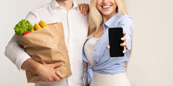 Нерозпізнані подружжя, що показують сумку для зберігання екрану мобільного телефону, фон студії — стокове фото