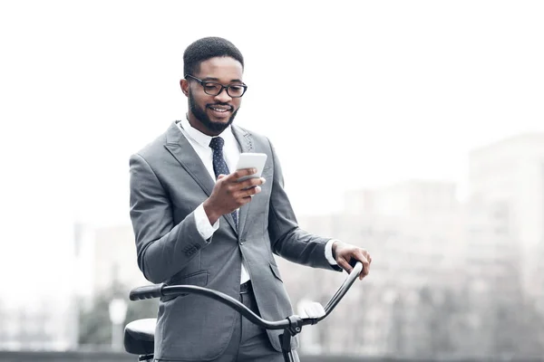 Ο άφρο επιχειρηματίας στέλνει μηνύματα στο τηλέφωνο, στέκεται με το ποδήλατο — Φωτογραφία Αρχείου
