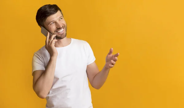 Homem feliz falando no telefone em pé no fundo amarelo — Fotografia de Stock