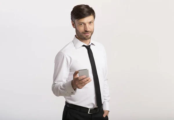 Чоловік тримає мобільний телефон стоячи на білому тлі — стокове фото