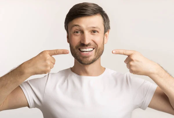 Uomo felice che punta le dita al suo sorriso perfetto, sfondo bianco — Foto Stock