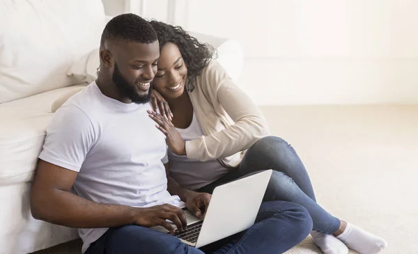 Happy black spouses sitting on floor with laptop