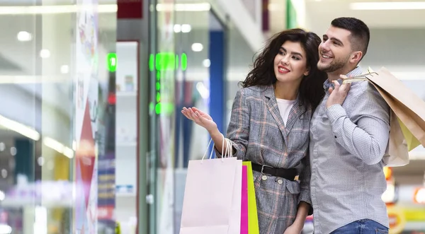 Mujer mostrando vestido nuevo en el escaparate, de compras con el marido —  Fotos de Stock