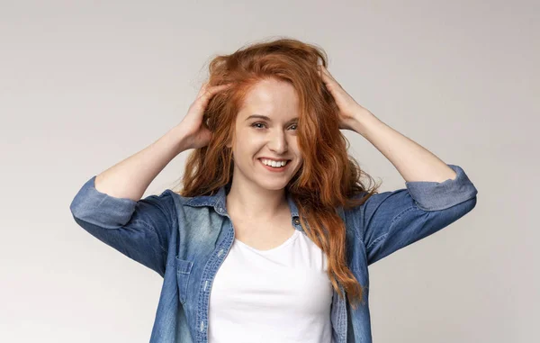 Chica pelirroja feliz sonriendo y tocando su hermoso pelo rizado — Foto de Stock