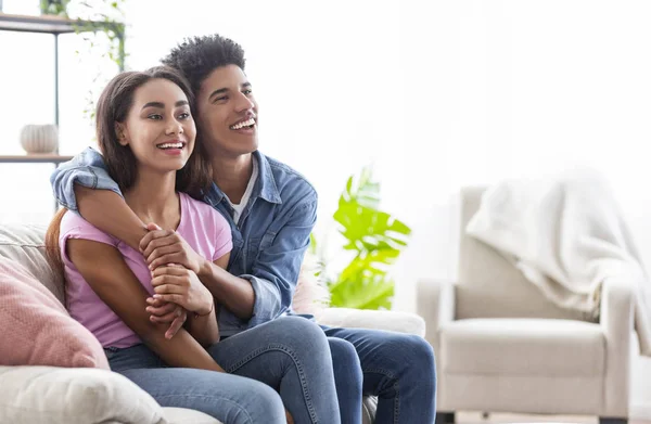 Svart glada tonåringar sitter på soffan, kramar och tittar åt sidan — Stockfoto