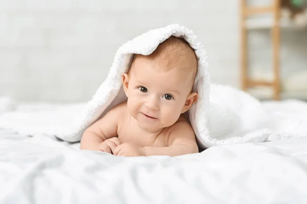 Милый мальчик ползает по кровати и прячется под одеялом. — стоковое фото