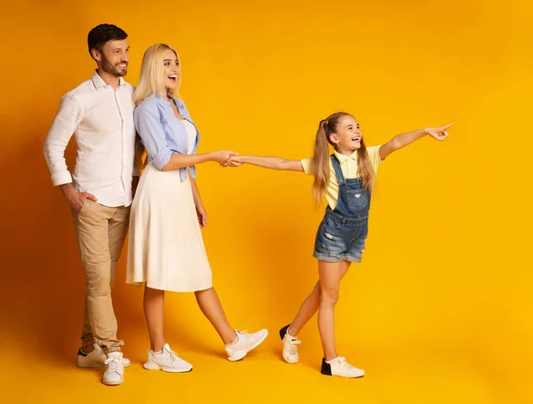 Filha apontando o dedo mostrando algo para os pais, fundo do estúdio amarelo — Fotografia de Stock