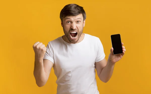Aufgeregter Mann zeigt Handybildschirm mit zitternden Fäusten, Studioaufnahme — Stockfoto
