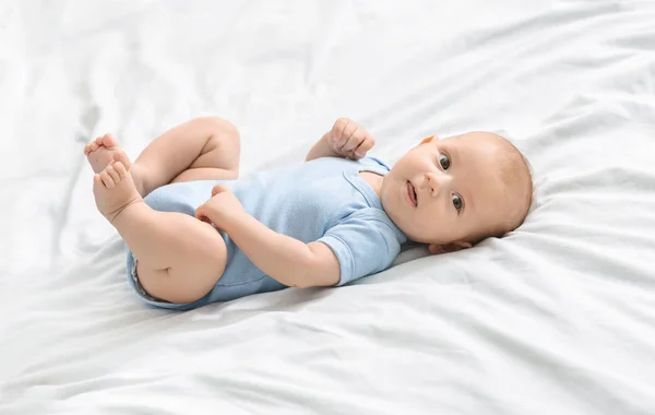 Mavi bodysuit yatakta yatan sevimli yenidoğan bebek — Stok fotoğraf
