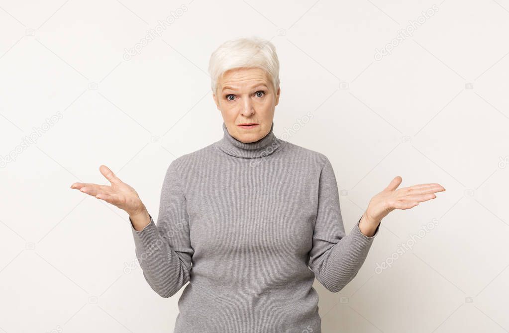 Displeased senior woman spreading hands and looking to camera