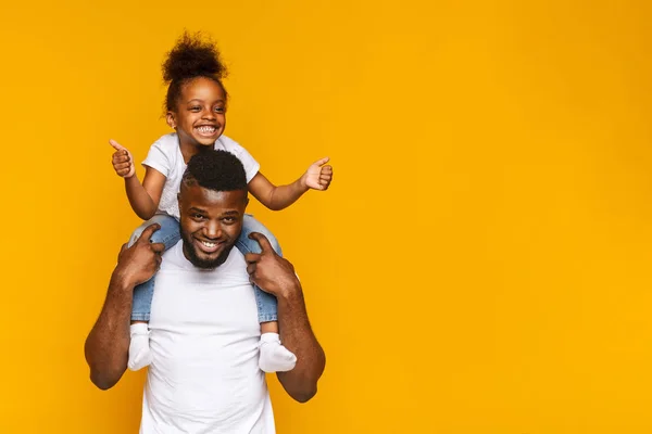 Adorável menina africana gesticulando polegares para cima nos ombros daddys — Fotografia de Stock