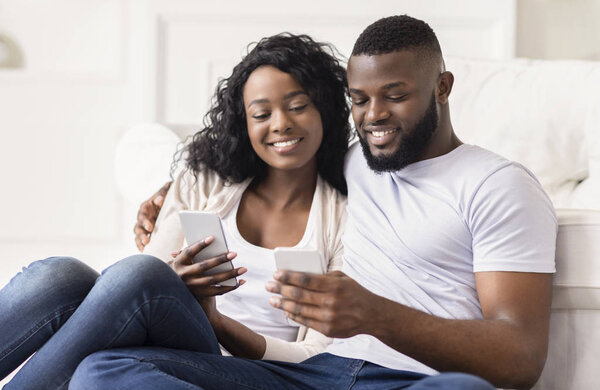 Smiling couple scrolling photos in smartphone together sitting at home
