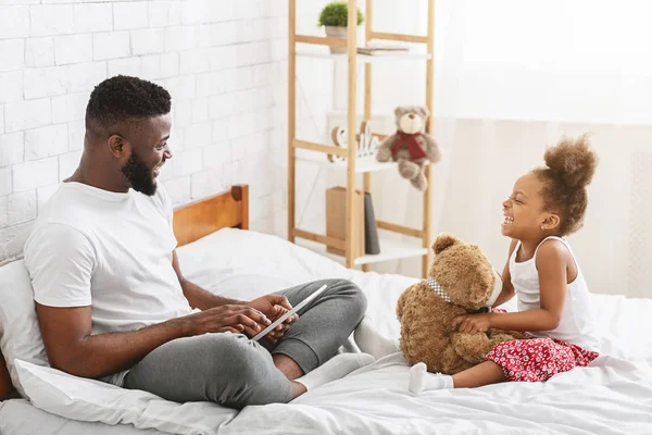 Hombre africano sentado en la cama con su hija, mirándose el uno al otro — Foto de Stock