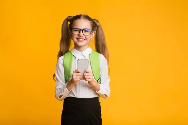 Schoolmeisje met behulp van mobiele telefoon over gele studio achtergrond — Stockfoto